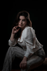 Young woman looking away while sitting against black background