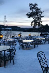 Empty chairs and tables at restaurant against sky during sunset