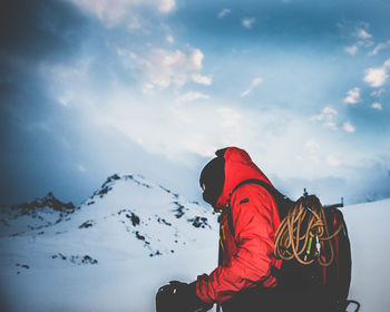 Side view of person standing on snowcapped mountain against cloudy sky