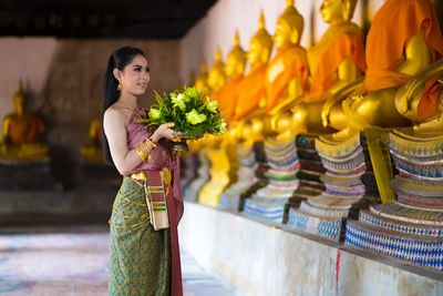 Woman holding flowers while standing by statues in temple