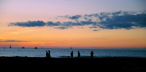 Silhouette people on beach against sky during sunset