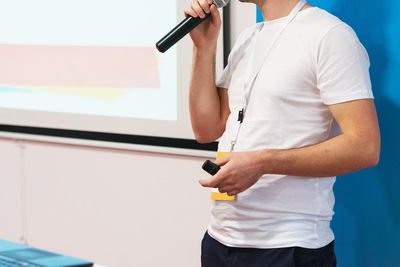 Midsection of man speaking on microphone while standing against wall