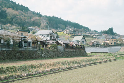 Houses on field by buildings against sky