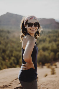 Smiling young woman standing on top of rock against mountains