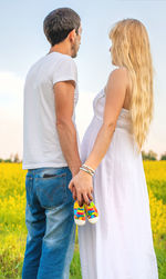 Couple holding baby shoes while standing on field