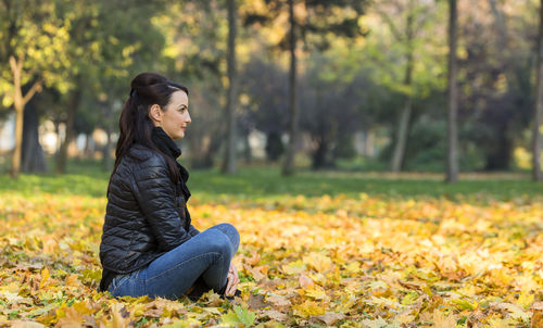 Side view of smiling young woman sitting on autumn leaves