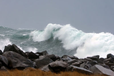 Waves splashing on rocks at shore against clear sky