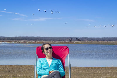 Full length portrait of young woman sitting at beach against sky