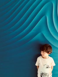 Boy looking away while standing by wall