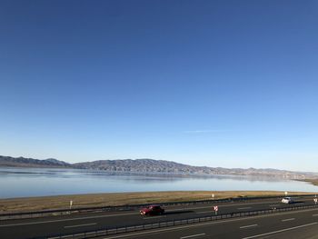 Road by sea against clear blue sky