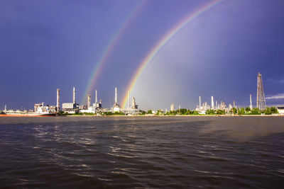 Scenic view of rainbow over sea and buildings against sky