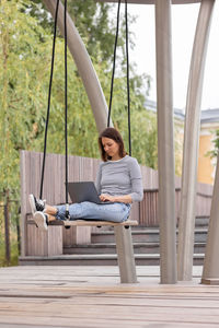 Woman with laptop sitting on swing