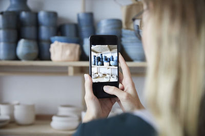 Cropped image of woman photographing earthenware with smart phone in art studio