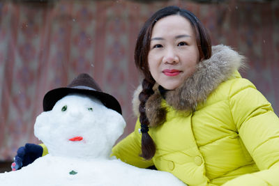 Portrait of smiling woman standing by snowman