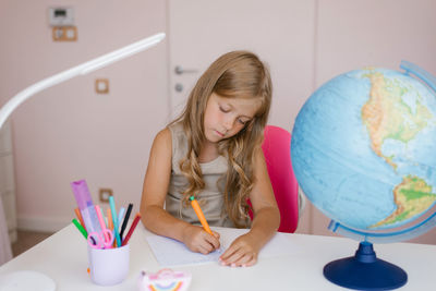 Small seven year old caucasian girl sitting at a table, writing school assignments by hand alone