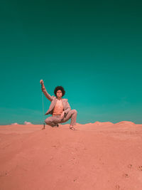 Full length of girl sitting on sand at beach against sky