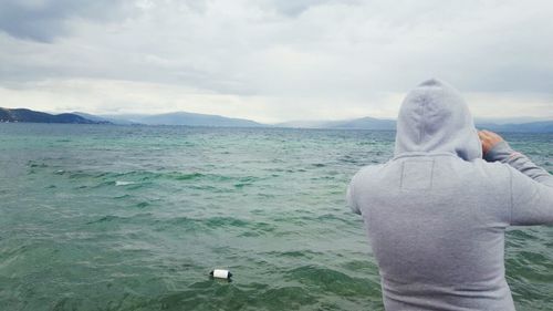 Rear view of man standing at beach against sky