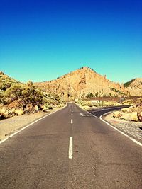 Empty road leading towards mountains against blue sky