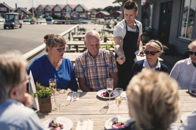 Young waiter serving food to senior friends at table on restaurant patio