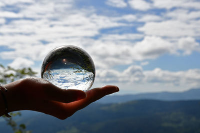 Reflection of person hand holding crystal ball against sky