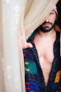 Portrait of man looking behind curtain at home