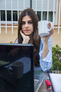 Portrait of woman with coffee cup and laptop on table