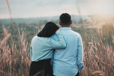 Rear view of couple standing on field against sky