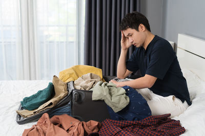 Side view of young man sitting on bed at home