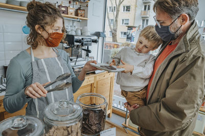 Female owner serving chocolate in plate to little by in candy store during pandemic