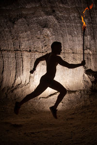 Full length of silhouette man running against rock formation