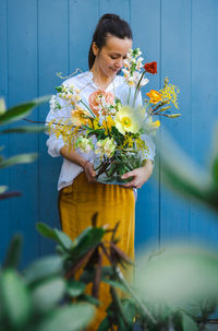 Young woman in flowing yellow skirt and white shirt with beautiful bouquet of peonies in glass vase