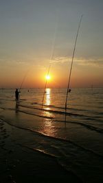 Silhouette man fishing at beach against sky during sunset