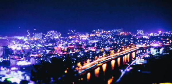 Illuminated bridge over river in city against sky at night