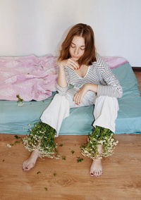 Young woman sitting with flowers on legs at home