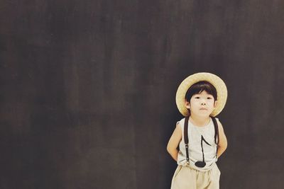 Close-up of cute boy standing against hat