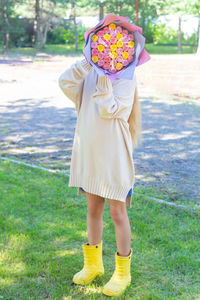 Caucasian girl in a long light sweater covered her face with a bouquet of multi-colored roses. 