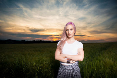 Beautiful young woman standing on field at sunset