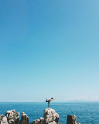 Mid distance view of woman practicing yoga while standing on rocks against sea and sky