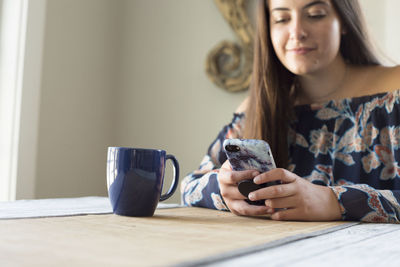 Young woman using phone while sitting on table