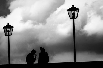 Silhouette people on street light against sky