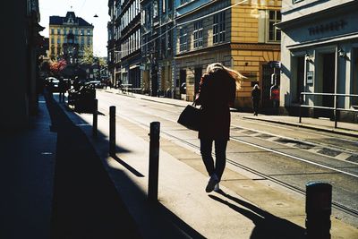 Rear view of woman walking on footpath in city