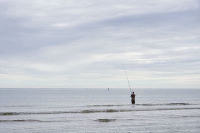 Man fishing on sea against cloudy sky