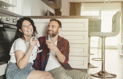 Smiling couple holding wineglass sitting at kitchen