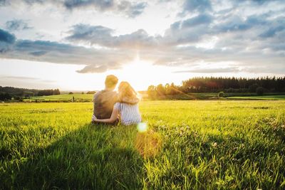 Rear view of couple sitting on field against sky