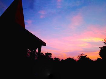 Low angle view of silhouette trees and buildings against sky during sunset