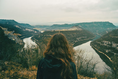 Rear view of woman looking at river amidst mountains against sky