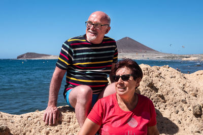 Smiling senior couple sitting on rock by sea