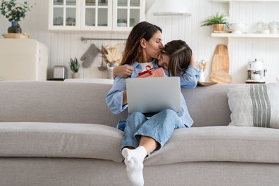 Young woman using phone while sitting on sofa at home