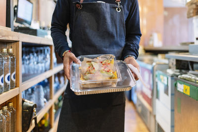 Mature male manager holding foil and plastic containers while working in restaurant