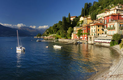 Boats on lake como by buildings against sky